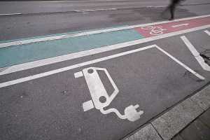 Ein Fußgänger geht über eine Straße, die an einen Radweg und einen Ladeparkplatz für Elektroautos in der Innenstadt grenzt. Um die CO2-Emissionen im Verkehrssektor möglichst schnell zu senken, hält Baden-Württembergs Verkehrsminister Hermann einen schnellen Ausbau der E-Mobilität für die beste Lösung. (Foto: Marijan Murat/dpa)