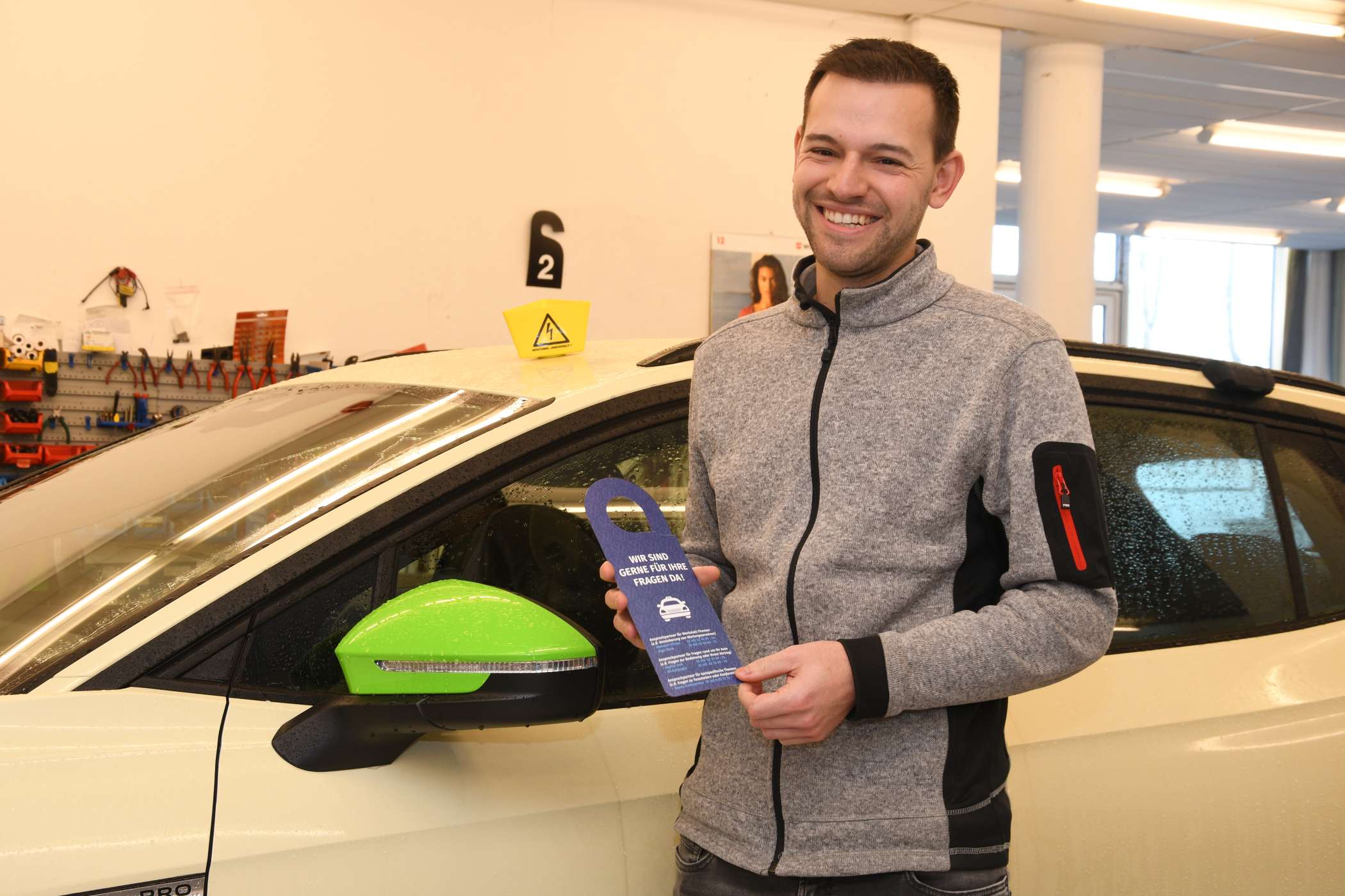 Juniorchef Felix Brandt zeigt einen Aufhänger für VW-Taxis, der für die Kunden gleich die Kontaktdaten der Ansprechpartner bei Volkswagen Automobile Hamburg und bei Reuss aufführt.