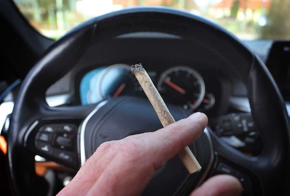 Ein Mann sitzt mit einem Joint zwischen den Fingern am Steuer eines Autos. (Foto: Karl-Josef Hildenbrand/dpa)